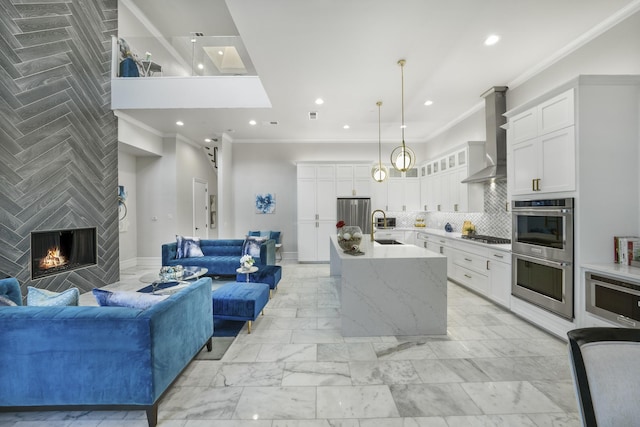 kitchen featuring appliances with stainless steel finishes, wall chimney range hood, pendant lighting, light stone counters, and a center island with sink