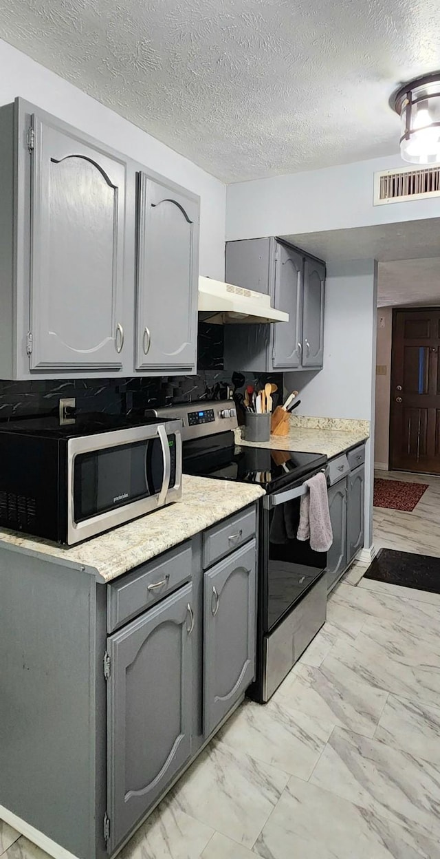 kitchen with tasteful backsplash, a textured ceiling, gray cabinetry, and appliances with stainless steel finishes