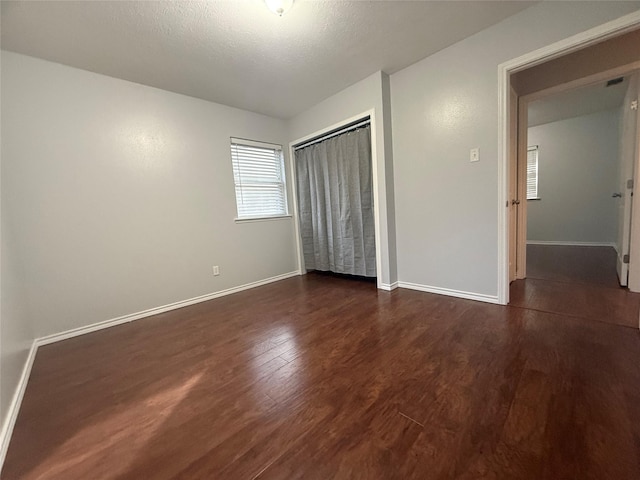 unfurnished bedroom featuring a textured ceiling, dark hardwood / wood-style flooring, and a closet