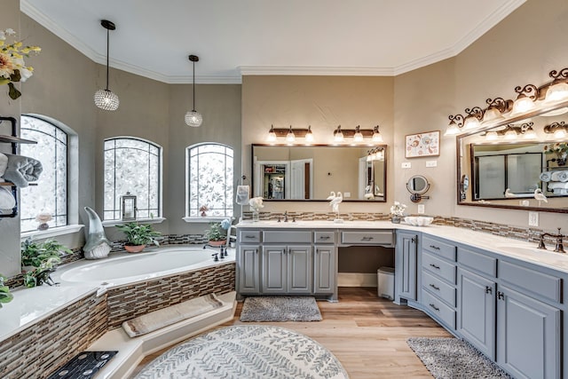 bathroom with ornamental molding, hardwood / wood-style floors, a relaxing tiled tub, and vanity