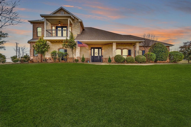 view of front of property with roof with shingles, brick siding, a balcony, and a lawn