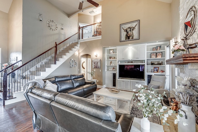 living area with a towering ceiling, dark wood-style floors, stairs, visible vents, and ceiling fan