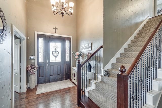 entryway with stairway, an inviting chandelier, a towering ceiling, and dark wood-style floors