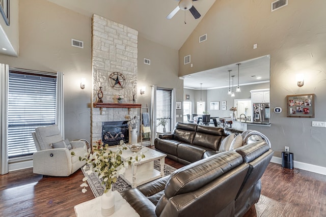 living room featuring a stone fireplace, crown molding, high vaulted ceiling, dark hardwood / wood-style flooring, and ceiling fan