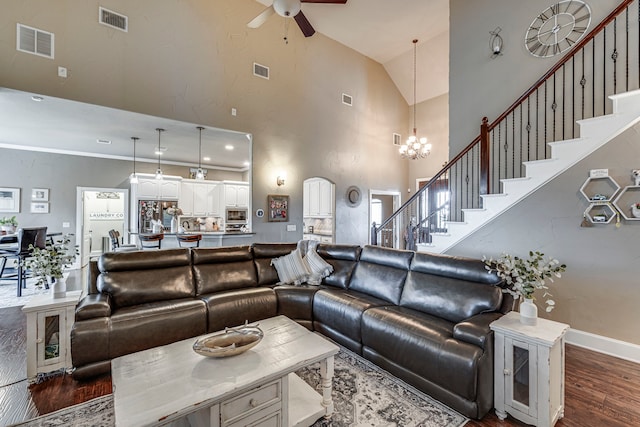 living room with dark wood-type flooring, ceiling fan with notable chandelier, and high vaulted ceiling