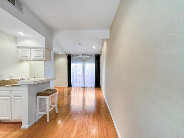 kitchen featuring kitchen peninsula, decorative light fixtures, light hardwood / wood-style floors, white cabinets, and a breakfast bar area