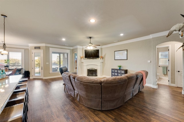 living room featuring arched walkways, dark wood finished floors, ceiling fan, crown molding, and a fireplace