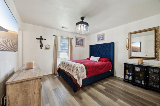 bedroom with hardwood / wood-style floors, an inviting chandelier, and a textured ceiling