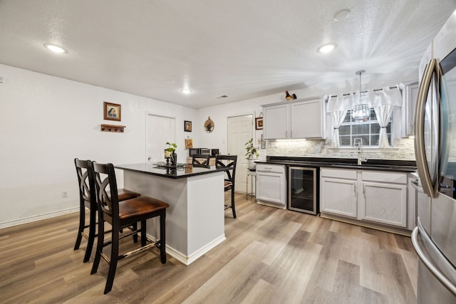 kitchen featuring white cabinets, a kitchen island, wine cooler, a kitchen breakfast bar, and hanging light fixtures