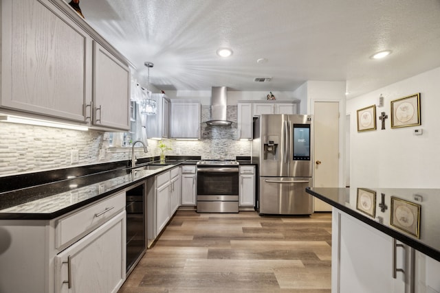 kitchen featuring pendant lighting, appliances with stainless steel finishes, beverage cooler, wall chimney exhaust hood, and sink