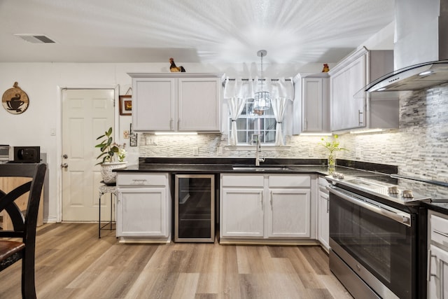 kitchen featuring stainless steel electric stove, white cabinets, beverage cooler, wall chimney range hood, and hanging light fixtures