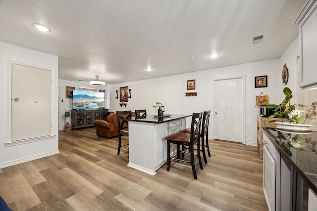 kitchen with a textured ceiling, white cabinets, a kitchen bar, and light wood-type flooring