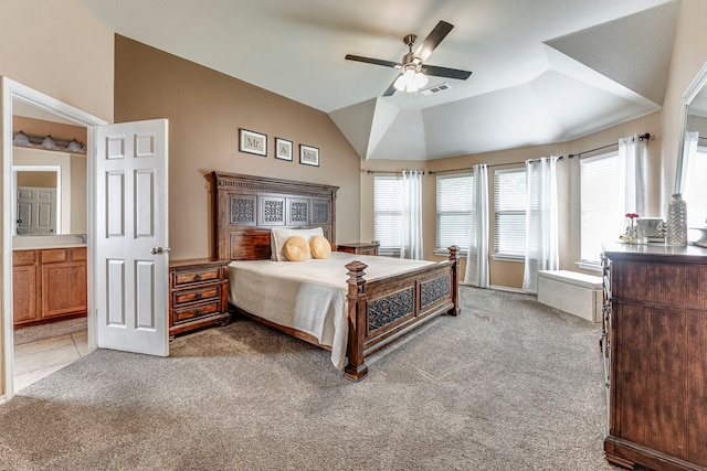 bedroom featuring ceiling fan, light colored carpet, vaulted ceiling, and ensuite bath