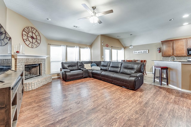 living room with ceiling fan, hardwood / wood-style floors, a fireplace, sink, and vaulted ceiling