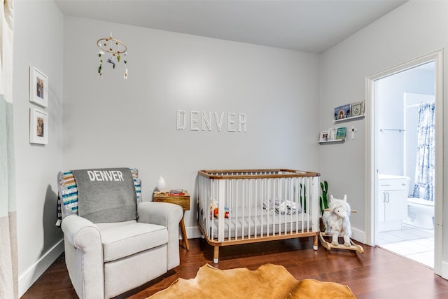 bedroom featuring connected bathroom, hardwood / wood-style floors, and a crib