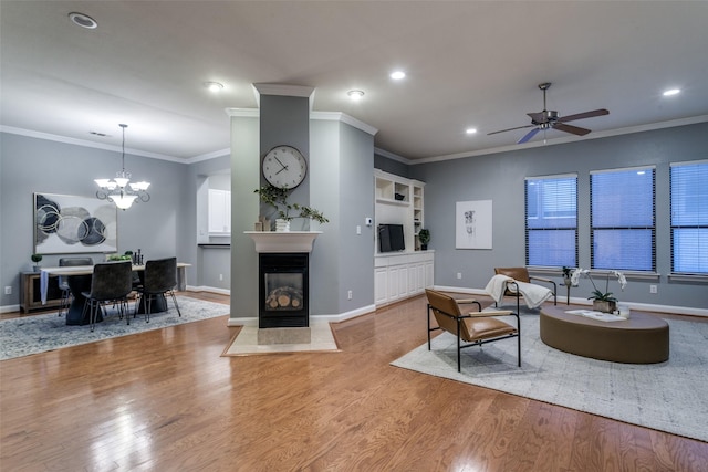 living room featuring built in features, ornamental molding, ceiling fan with notable chandelier, a multi sided fireplace, and light hardwood / wood-style floors