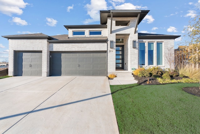 prairie-style house featuring an attached garage, a front lawn, concrete driveway, and brick siding