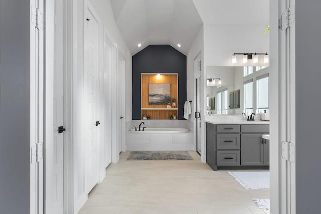 bathroom featuring tiled tub, vanity, and lofted ceiling