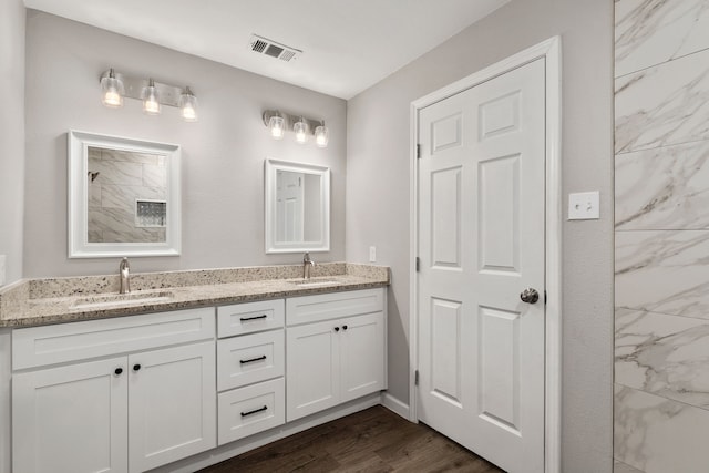 full bath with double vanity, visible vents, a sink, and wood finished floors