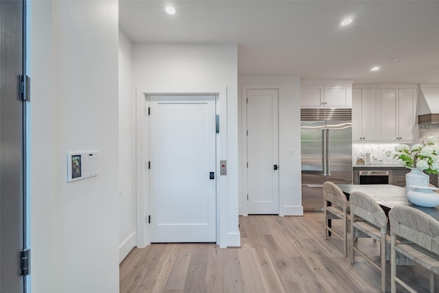 kitchen with built in refrigerator, white cabinetry, light hardwood / wood-style flooring, and tasteful backsplash