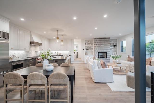 kitchen with pendant lighting, white cabinetry, light hardwood / wood-style flooring, custom range hood, and high quality appliances