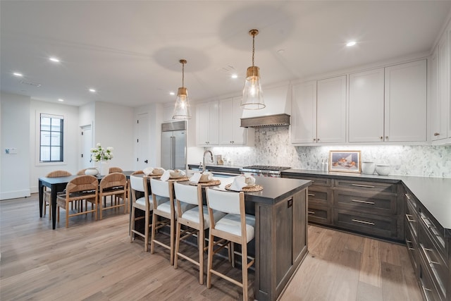 kitchen featuring pendant lighting, white cabinetry, stainless steel built in refrigerator, light hardwood / wood-style floors, and a center island with sink