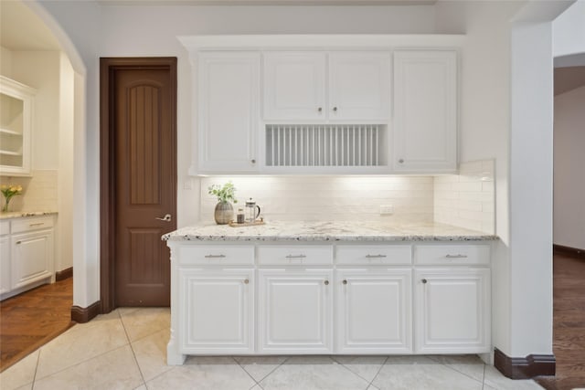 kitchen featuring white cabinetry, light tile patterned floors, backsplash, and light stone counters