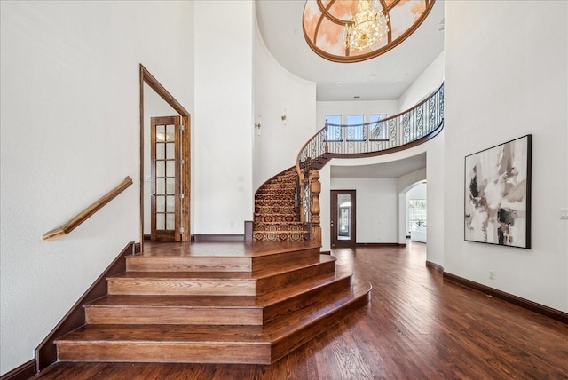 staircase with a towering ceiling, a chandelier, and hardwood / wood-style flooring