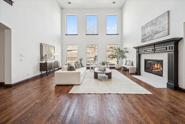 living room featuring a tile fireplace, dark wood-type flooring, and a towering ceiling