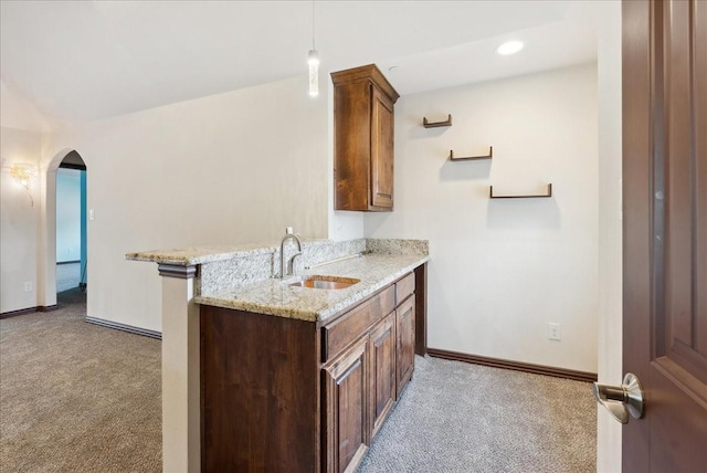 kitchen featuring sink, hanging light fixtures, kitchen peninsula, light colored carpet, and light stone countertops