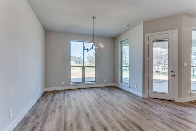 unfurnished dining area featuring a notable chandelier, wood finished floors, visible vents, and baseboards