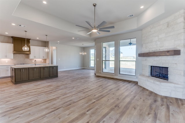 unfurnished living room with visible vents, light wood-type flooring, a stone fireplace, a raised ceiling, and a sink