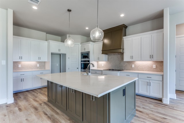 kitchen featuring stainless steel appliances, a sink, custom exhaust hood, white cabinetry, and a large island with sink