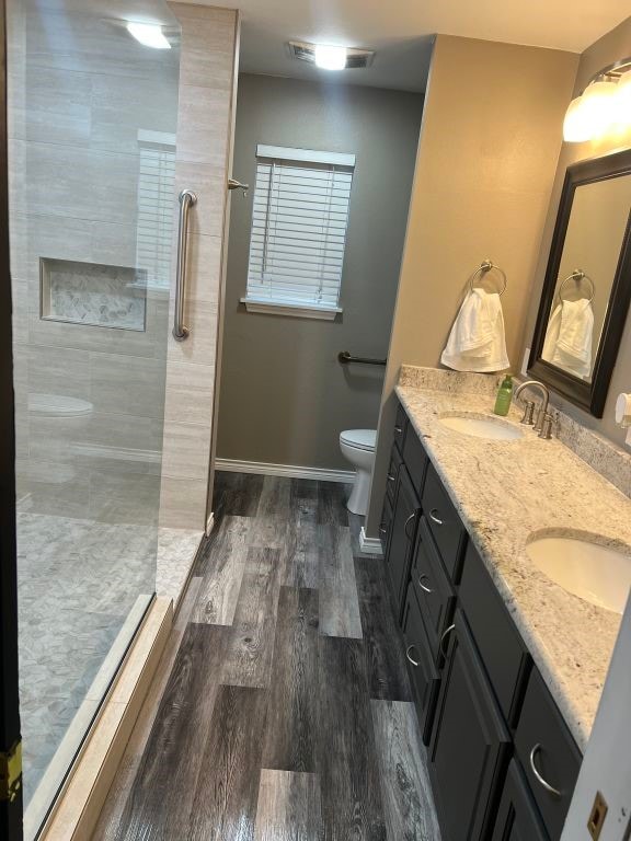 bathroom with a tile shower, hardwood / wood-style floors, toilet, and vanity