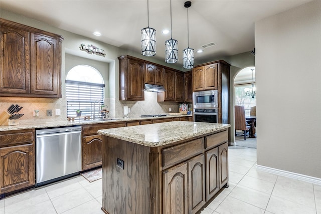 kitchen featuring appliances with stainless steel finishes, hanging light fixtures, sink, a kitchen island, and dark brown cabinetry