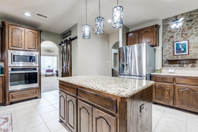 kitchen with pendant lighting, appliances with stainless steel finishes, a center island, light colored carpet, and a barn door