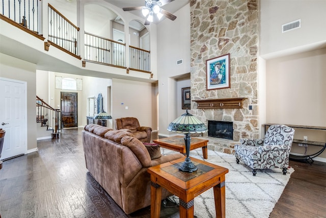 living room with a towering ceiling, ceiling fan, dark hardwood / wood-style floors, and a fireplace