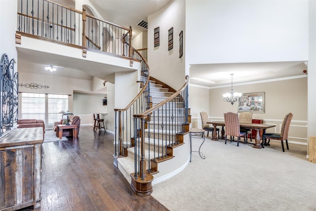 stairway with a chandelier, hardwood / wood-style floors, ornamental molding, and a towering ceiling