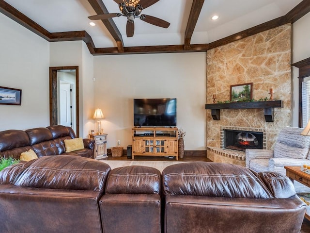 living room with ceiling fan, beamed ceiling, and a stone fireplace