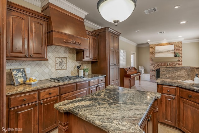 kitchen featuring premium range hood, stainless steel gas cooktop, dark stone countertops, and crown molding