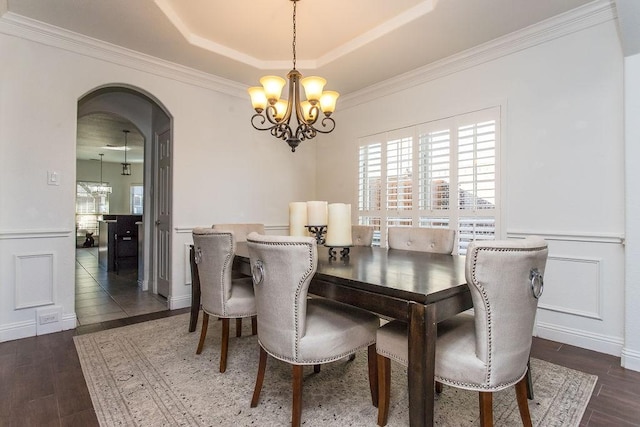 dining area featuring dark wood-type flooring, a tray ceiling, crown molding, and a notable chandelier