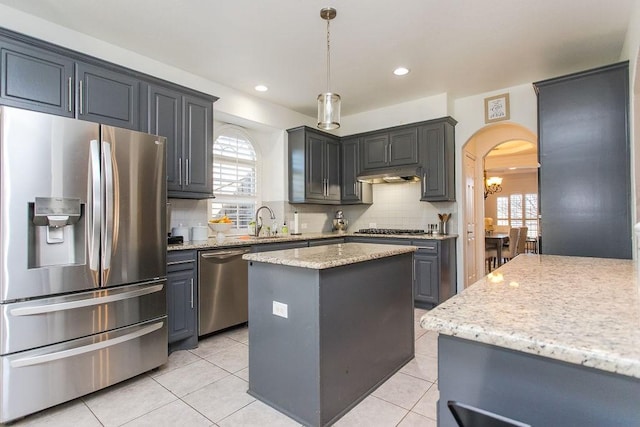 kitchen with pendant lighting, light stone countertops, a center island, decorative backsplash, and stainless steel appliances