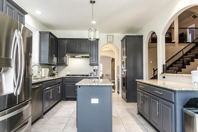 kitchen with appliances with stainless steel finishes, a center island, decorative light fixtures, decorative backsplash, and sink