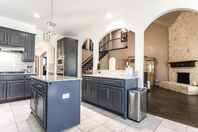 kitchen with a fireplace, a kitchen island, pendant lighting, backsplash, and stainless steel appliances