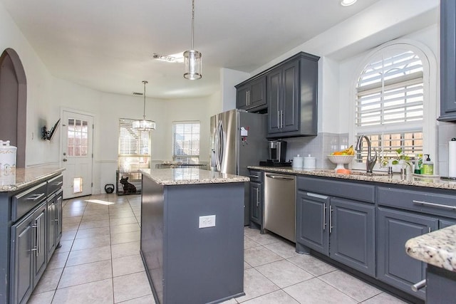 kitchen with light stone countertops, a center island, decorative light fixtures, stainless steel appliances, and light tile patterned floors