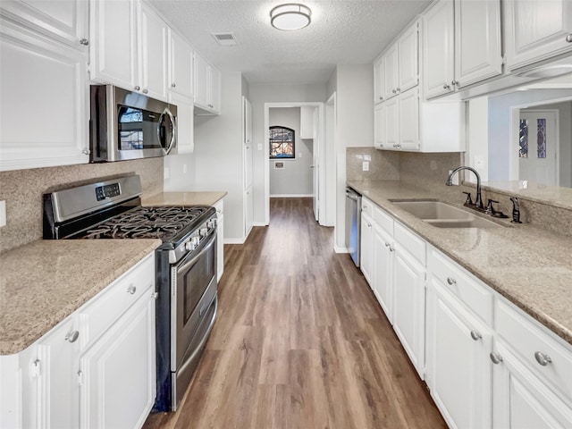 kitchen with sink, appliances with stainless steel finishes, hardwood / wood-style floors, a textured ceiling, and white cabinets