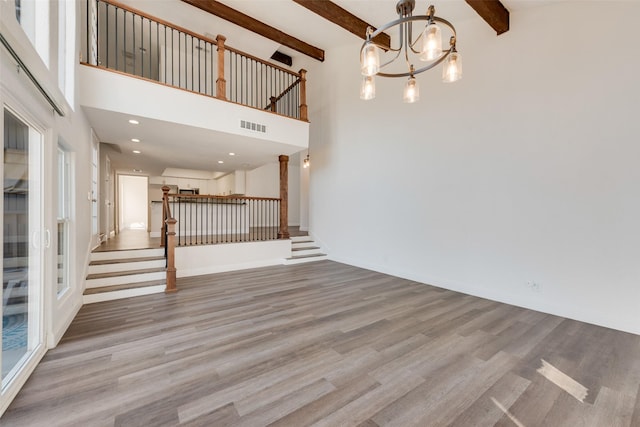 unfurnished living room with plenty of natural light, light hardwood / wood-style flooring, beamed ceiling, and a notable chandelier