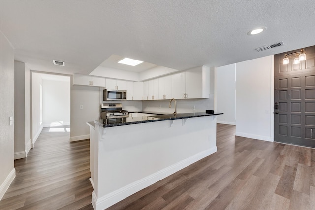 kitchen featuring a textured ceiling, appliances with stainless steel finishes, white cabinetry, light hardwood / wood-style flooring, and a breakfast bar area