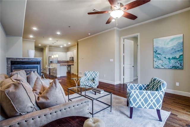 living room with hardwood / wood-style flooring, ceiling fan, ornamental molding, and a fireplace