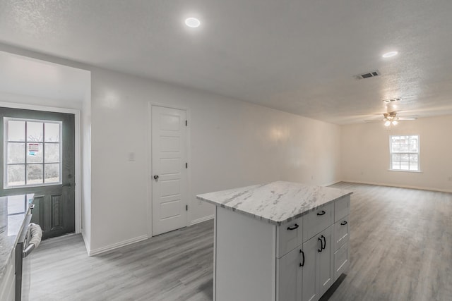 kitchen featuring light stone countertops, white cabinets, light wood-type flooring, and a kitchen island